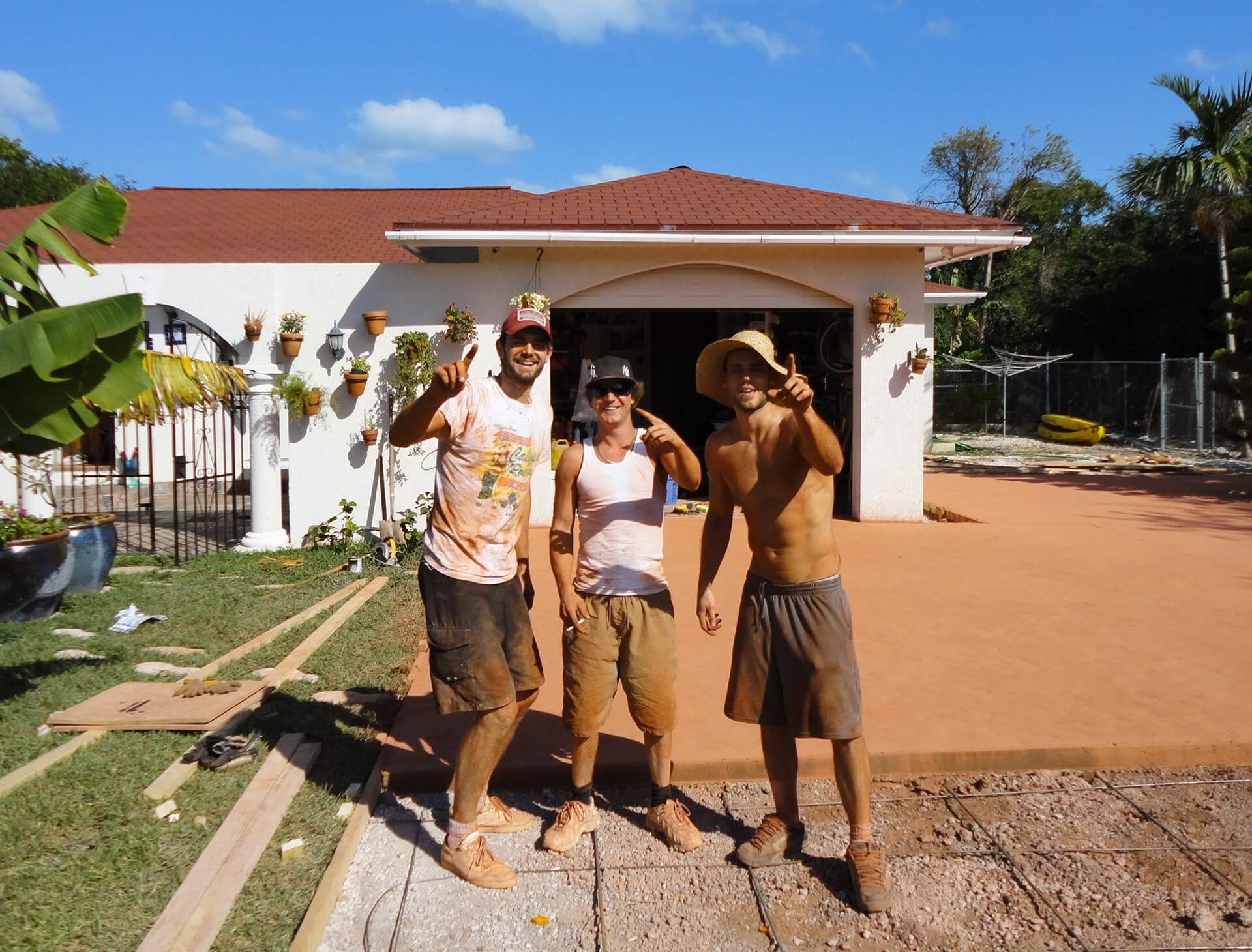 Three concrete workers pose with one finger in the air showing one pour remaining on a large driveway project in Nassau, Bahamas.