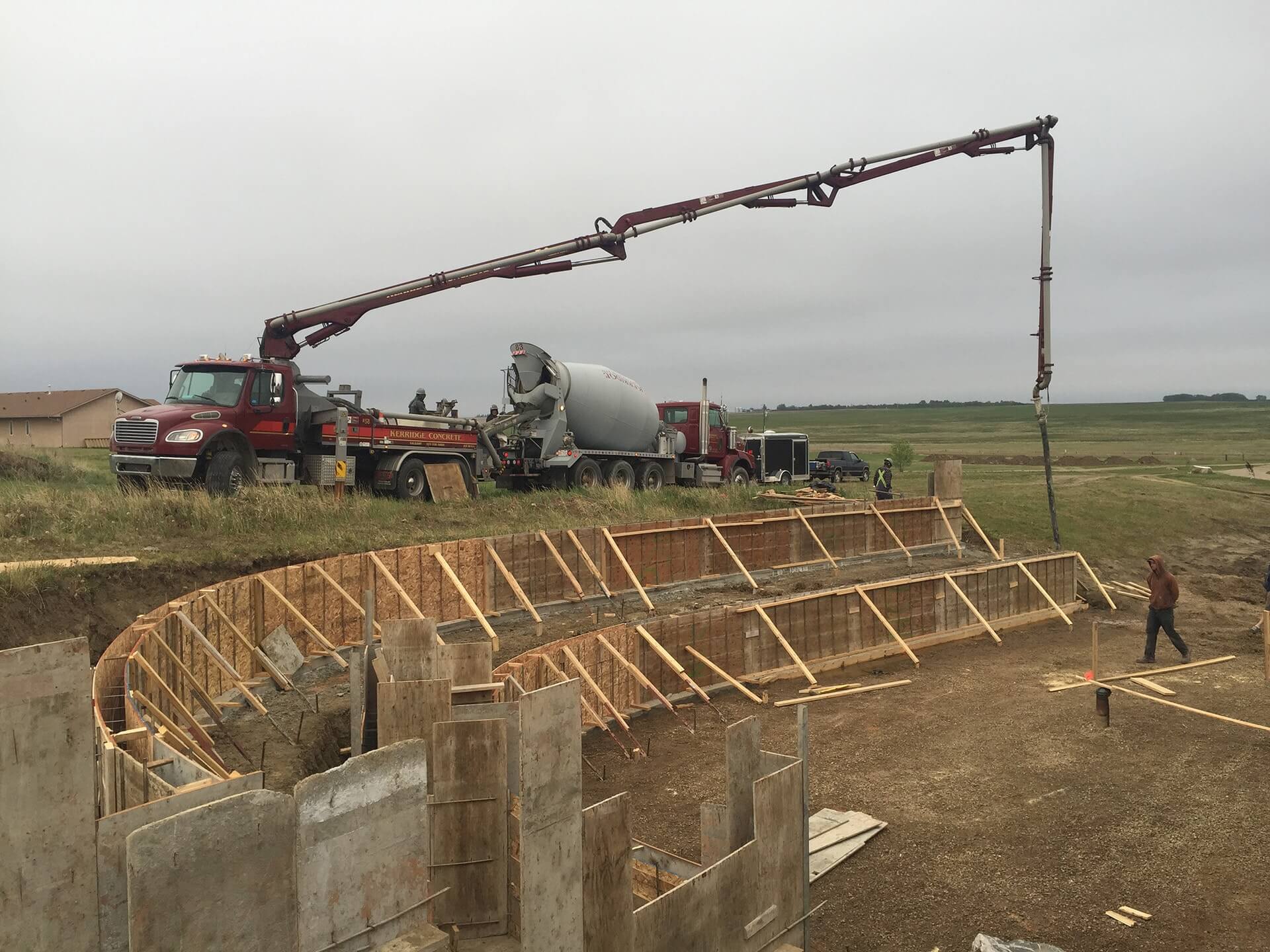 A concrete boom pump prepares to place concrete in two curved retaining walls.