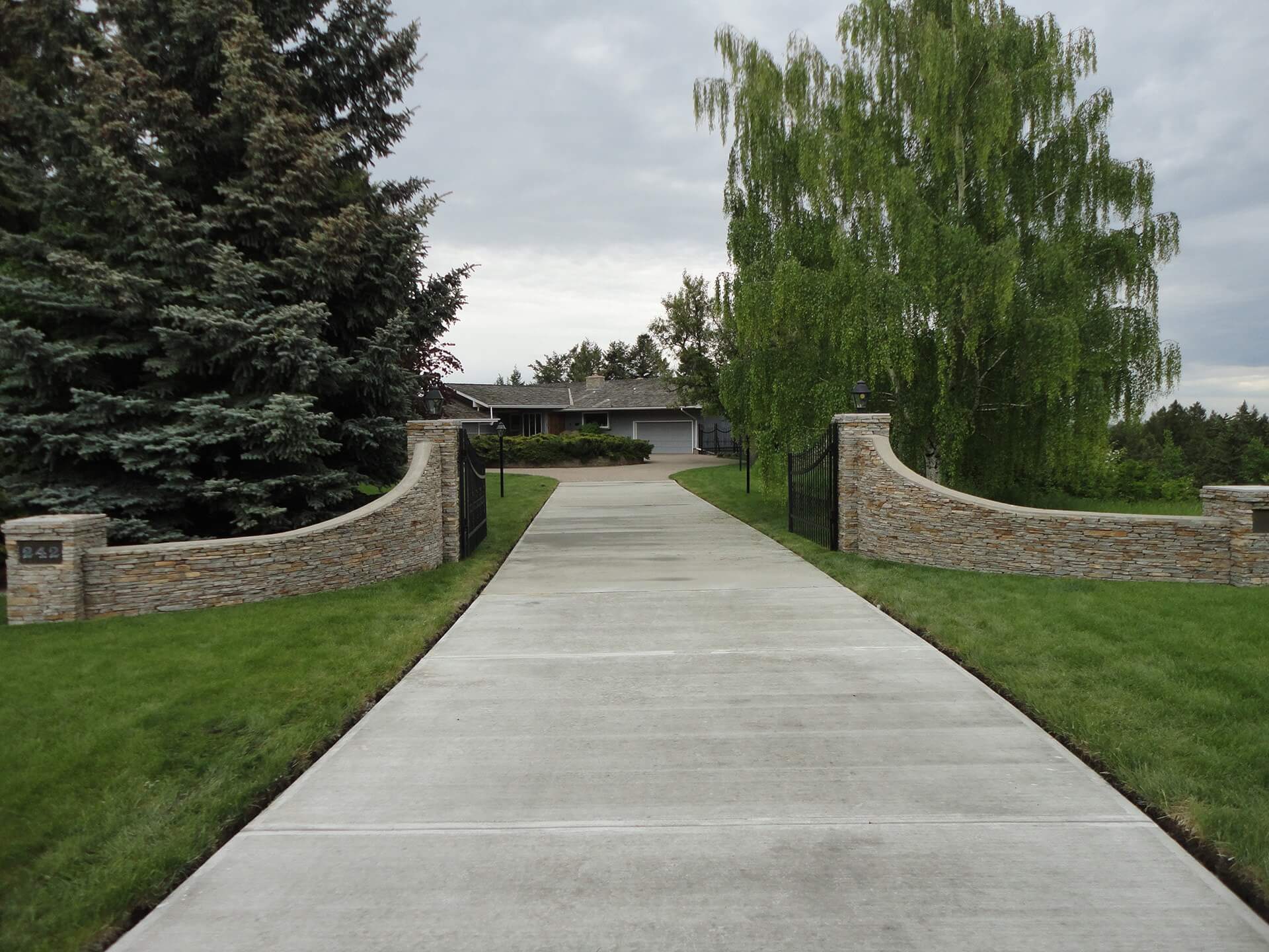 An open property gate shows an inviting entrance along a long concrete driveway.