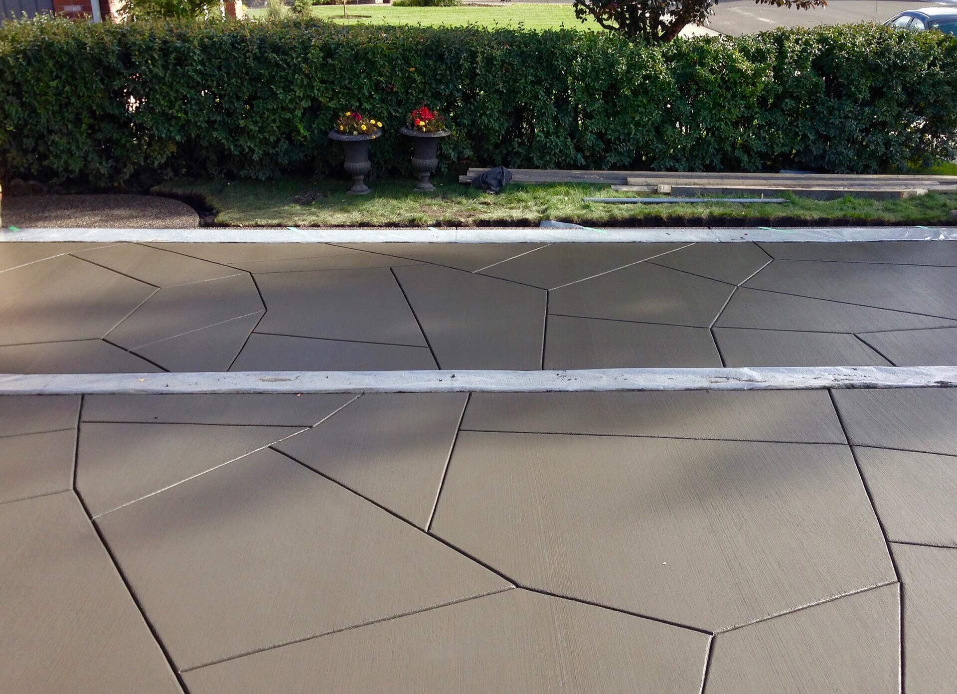Unique, five sided shapes have been hand cut into a brushed driveway to achieve a custom design. Border areas remain covered in plastic to protect them during the work.