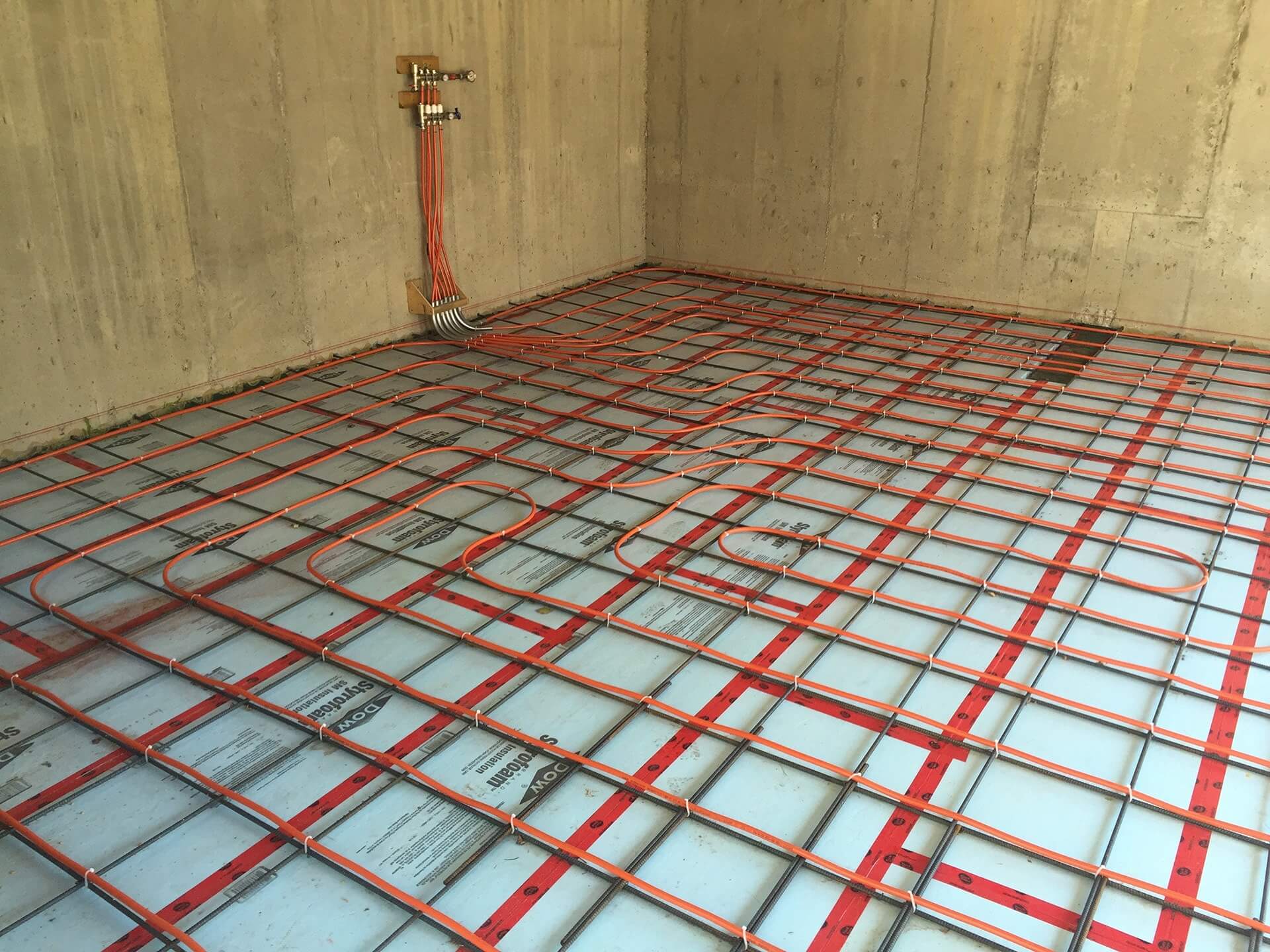 An engineered garage floor is prepared for concrete. Rigid foam insulation sits beneath a tight rebar grid and red piping for in floor heating.