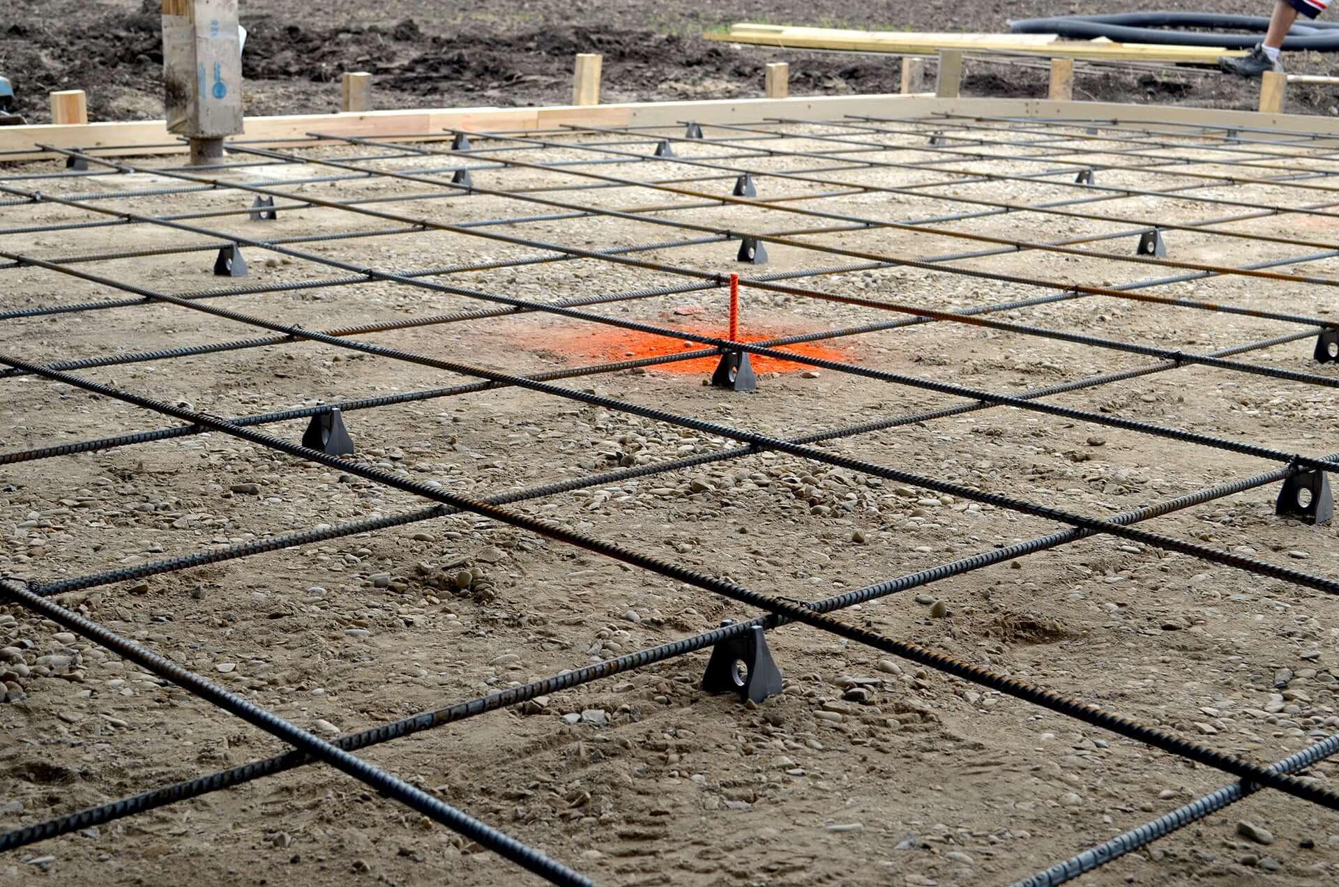 Compacted gravel and 10mm rebar are set for a concrete pour. The rebar is chaired off the ground for proper placement in the concrete and an orange height pin shows the ideal top of slab.