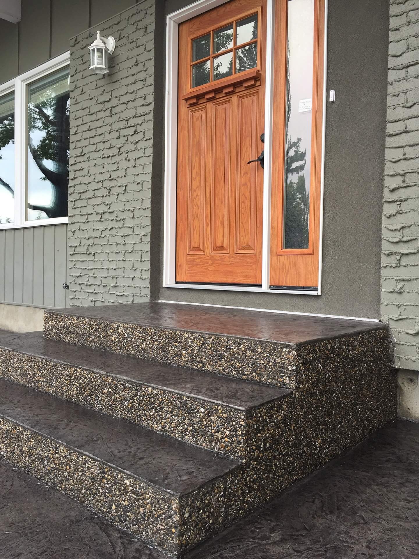 A stamped concrete front step with exposed aggregate frames a natural wood front door.