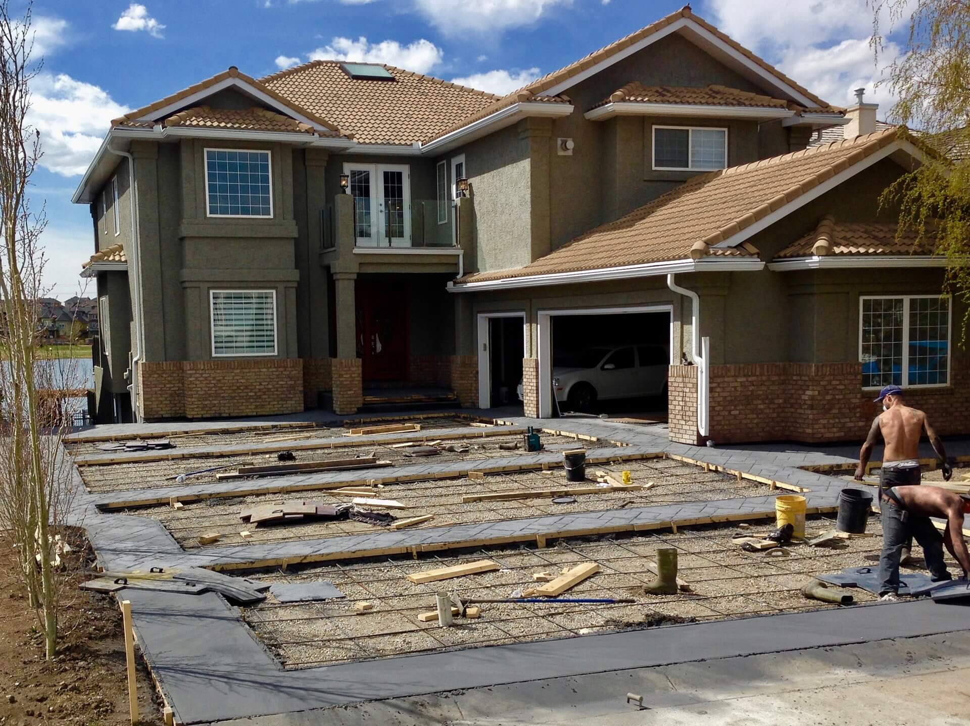 Concrete finishers work to complete the stamping process on a large driveway.