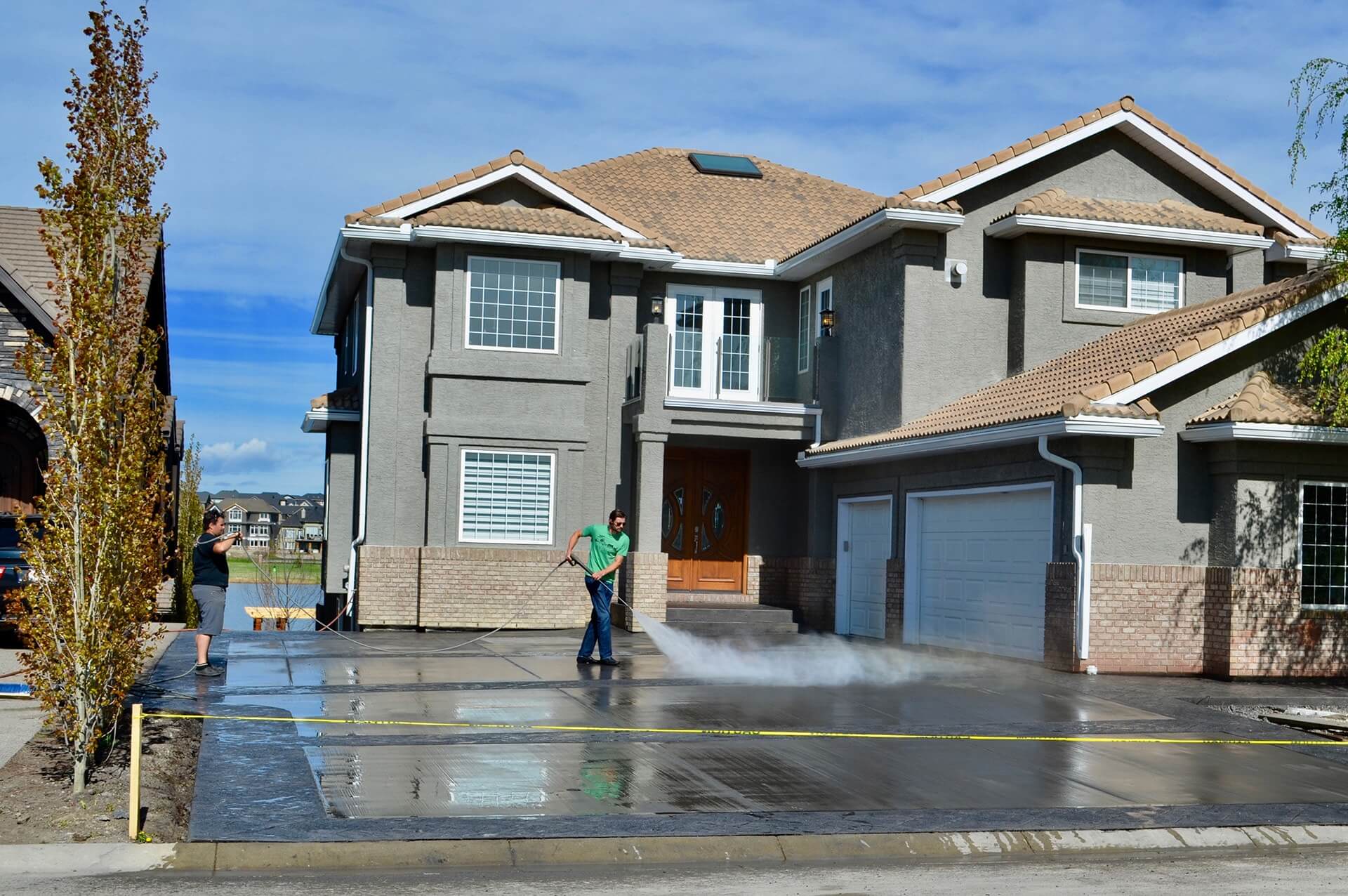 A concrete worker pressure washes a new driveway to water cure it.