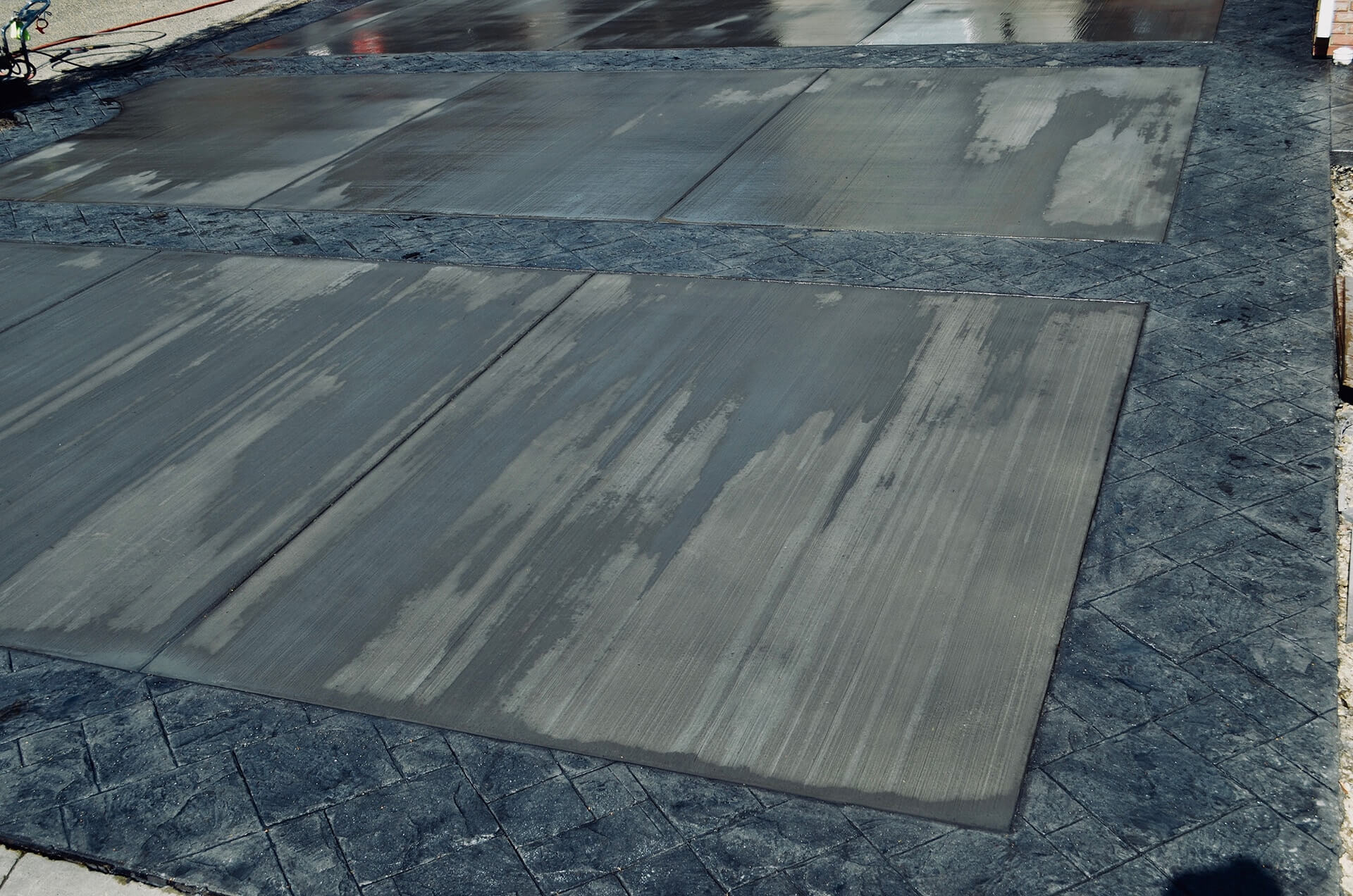 Close up of a new driveway. It has stamped borders and the inserts are brushed finish concrete with no highlights on the edges. Referred to in the industry as a "California Broom".