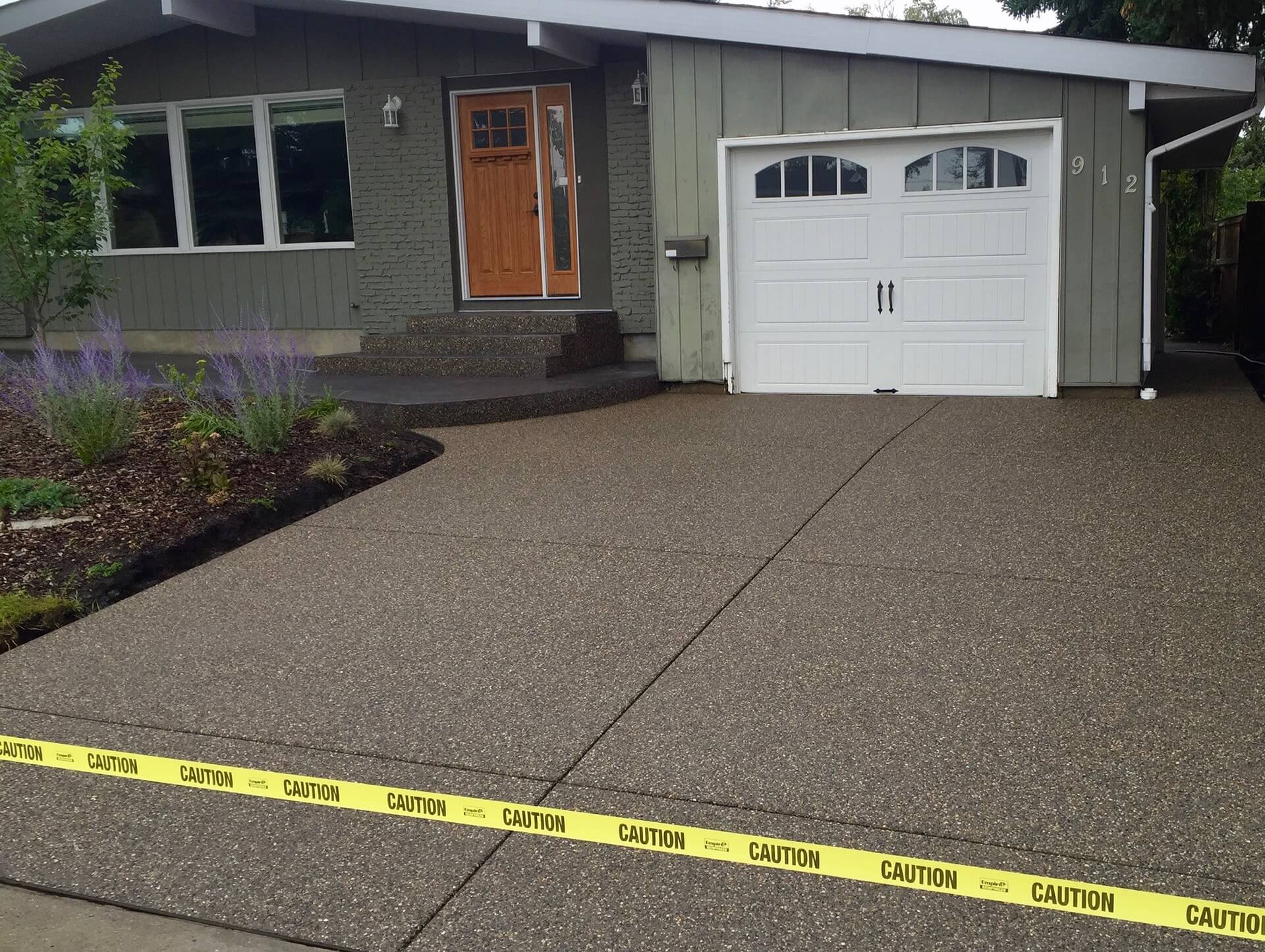 Yellow caution tape flags off the front of a newly made exposed aggregate driveway.