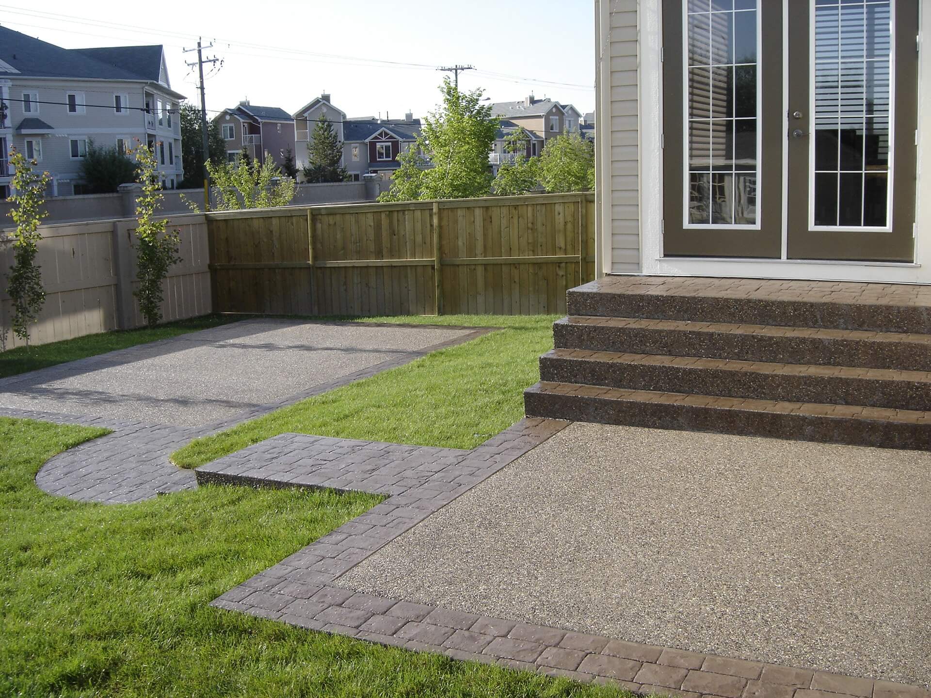 A brown bi-level concrete patio finished in exposed aggregate with stamped concrete borders.