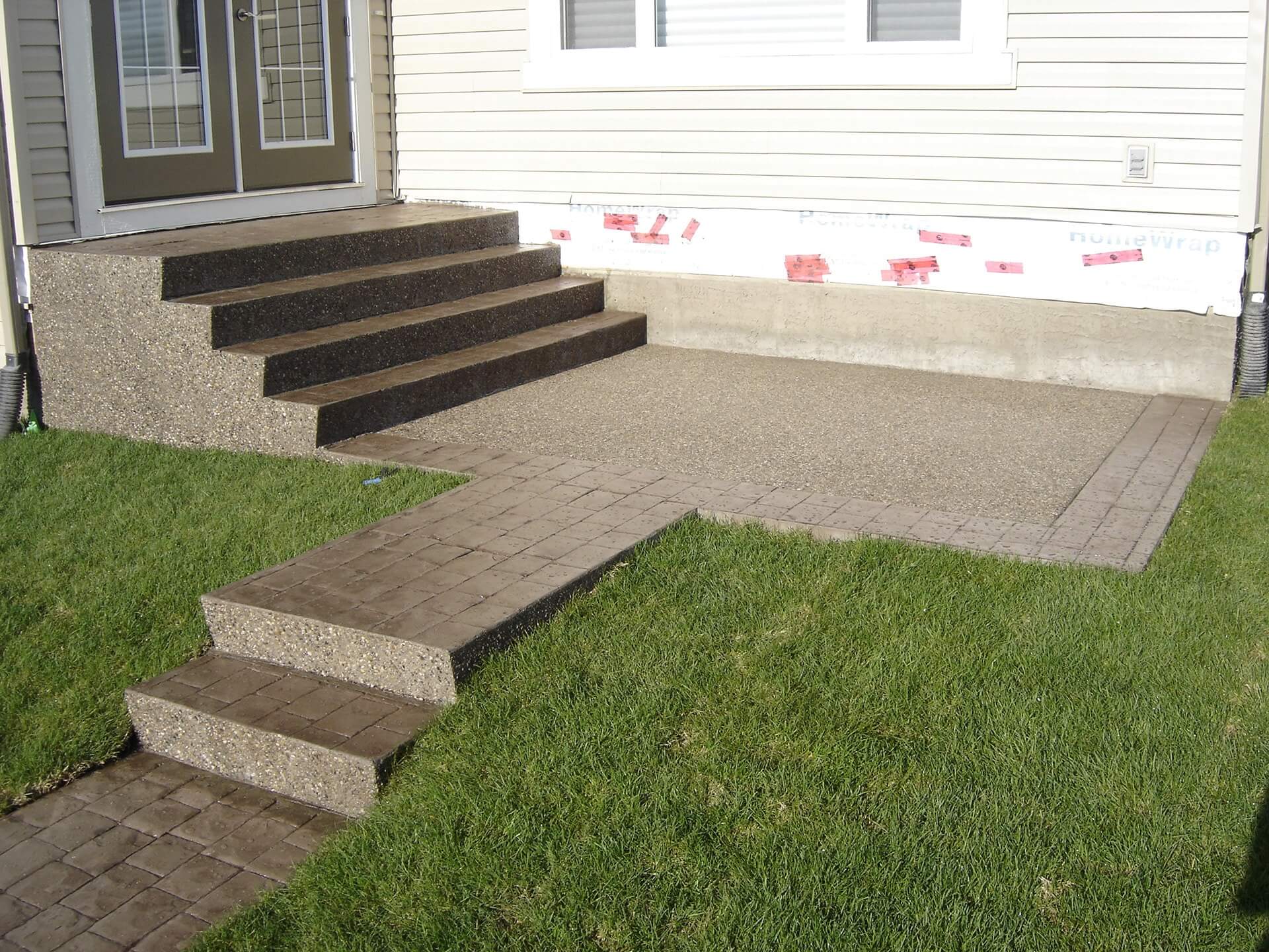 Exposed aggregate steps from a back patio entrance of a home surrounded by new sod.