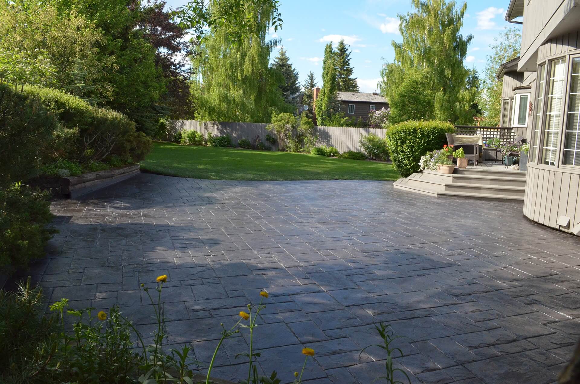 Stamped concrete patio in a large backyard with a wooden deck and mature trees.
