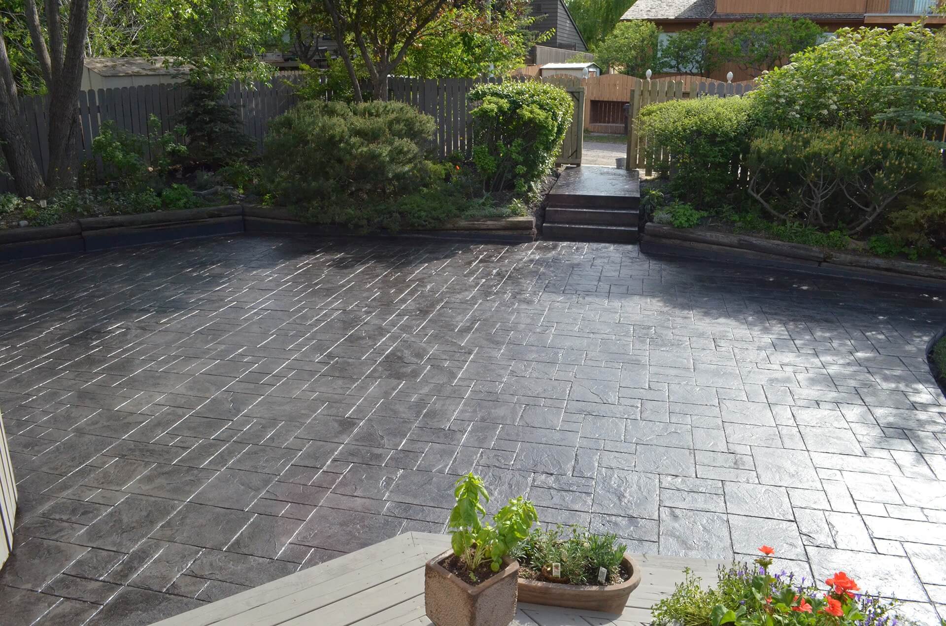 A shiny and beautiful stamped patio is set along a mature garden. The pattern of the stamp is called Grand Ashlar.