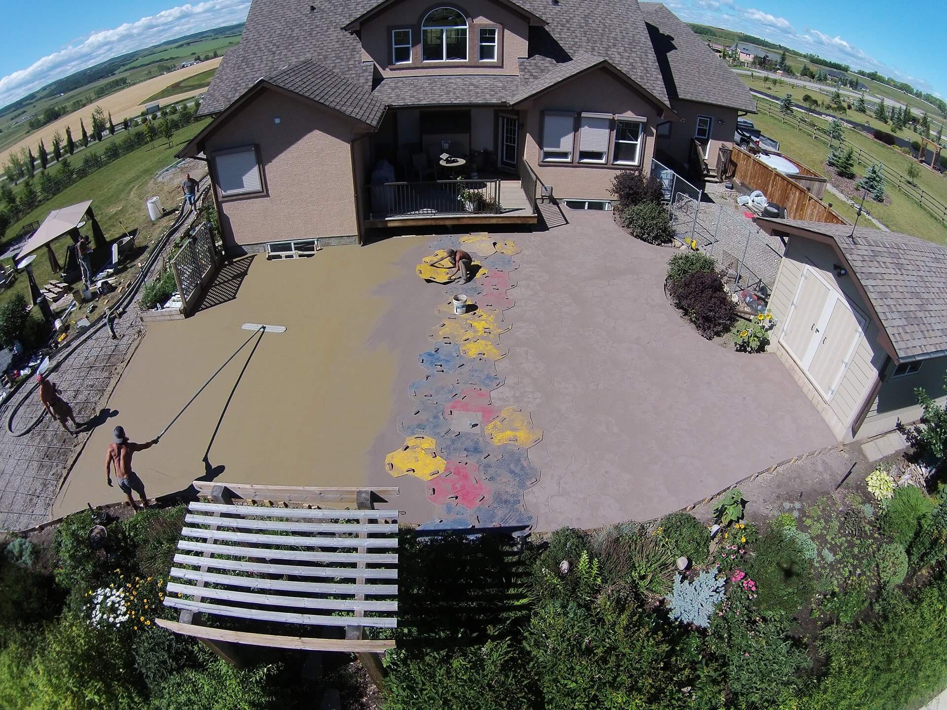 an aerial drone shot of a large patio being stamped. A worker impressions the concrete while another floats the surface in preparation for finishing.