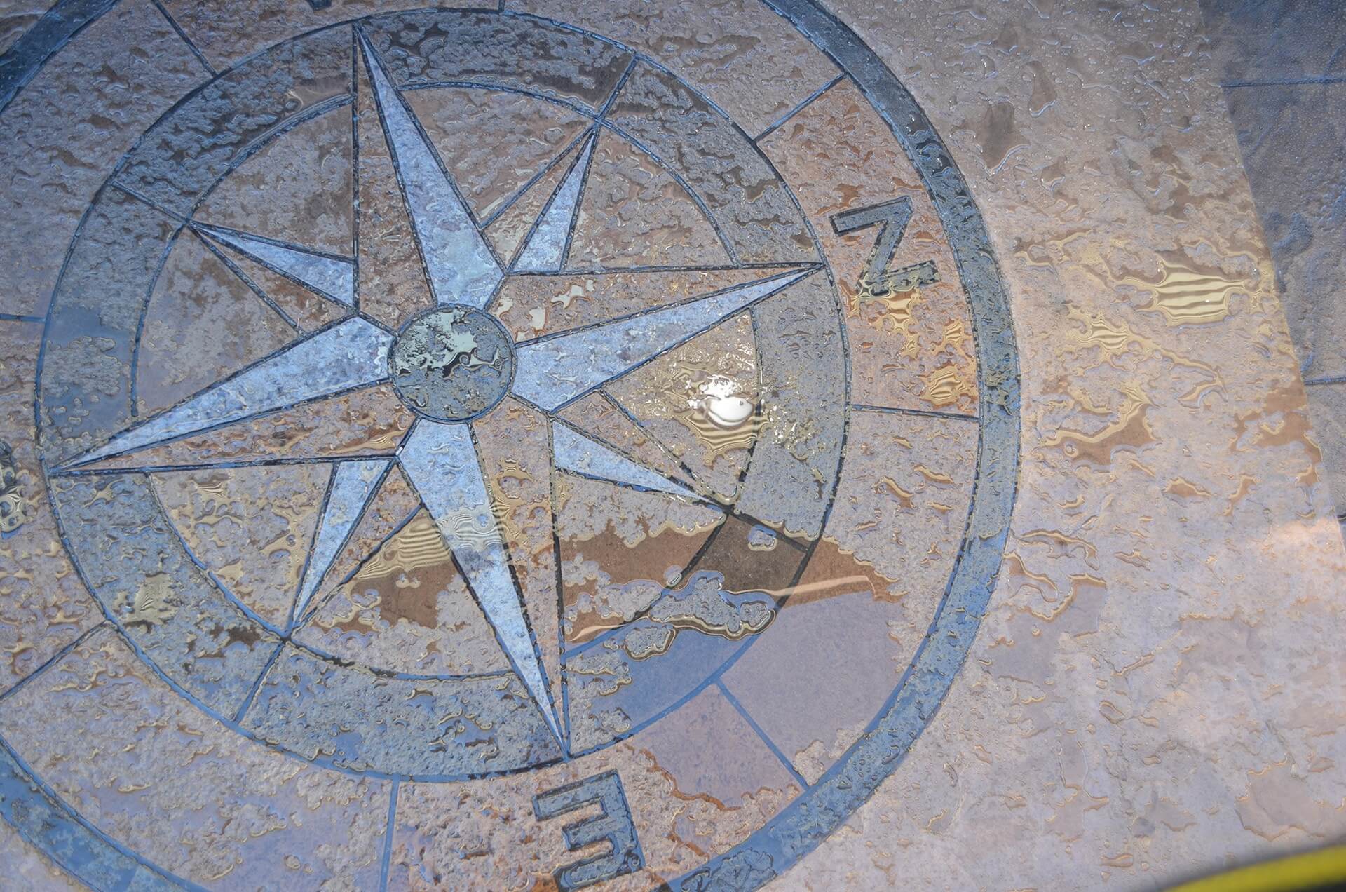 a hand stained compass rose has been stamped in concrete as a front step design.