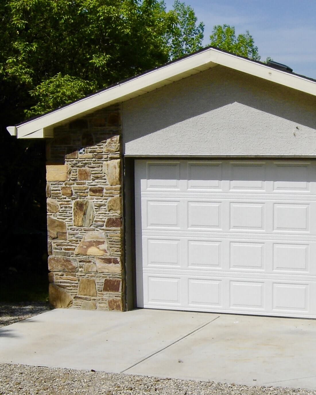 Single car garage finished with real stone and a large concrete apron approaching the main door.